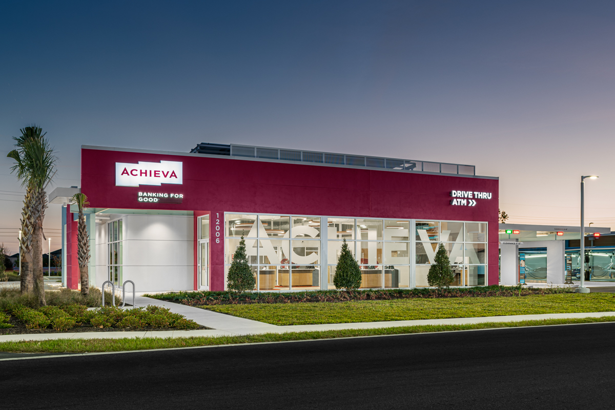 Achieva Credit Union Bank photo shot at night, highlighting the front exterior of the building. Solar panels peak from the roof of the building which is designed with large windows and a modern composition,